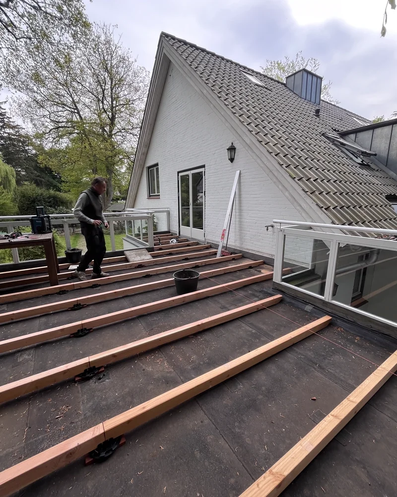 Zimmerer verlegt die Lagerhölzer einer Terrasse auf abgedichtetem Untergrund