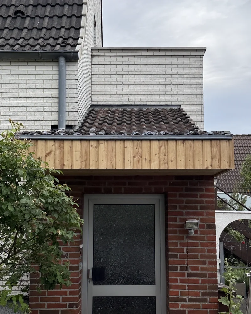 Vordach mit senkrechter Holzverkleidung über dem Eingang eines Klinkerhauses