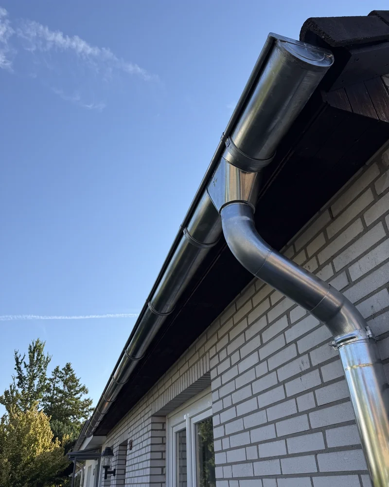 Neue Zinkdachrinne mit Fallrohr an einem Klinkerhaus vor blauem Himmel